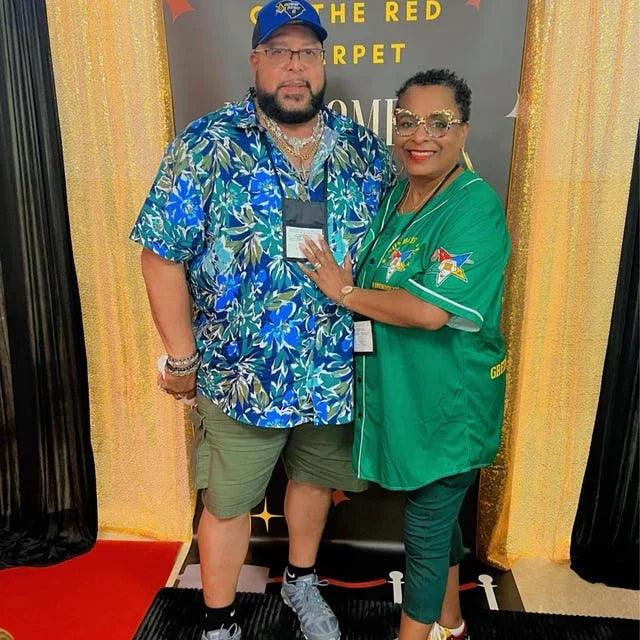 Two people posing together on a red carpet with a gold curtain background.