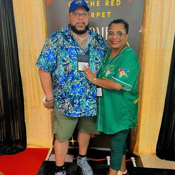 Two people posing together on a red carpet with a gold curtain background.